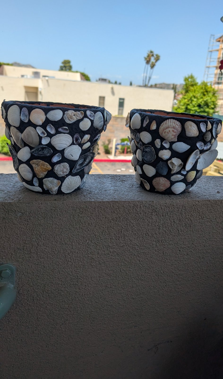 Two seashell-covered pots on a balcony ledge